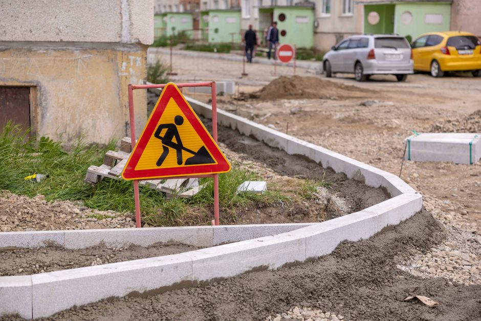 Imagem de uma área de construção ao ar livre com sinal de advertência para obras, indicando trabalhos de infraestrutura na via pública.