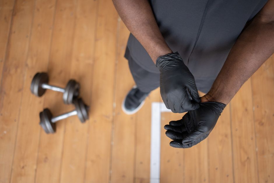 Pessoa colocando luvas de proteção antes de iniciar um treino de musculação em uma academia.