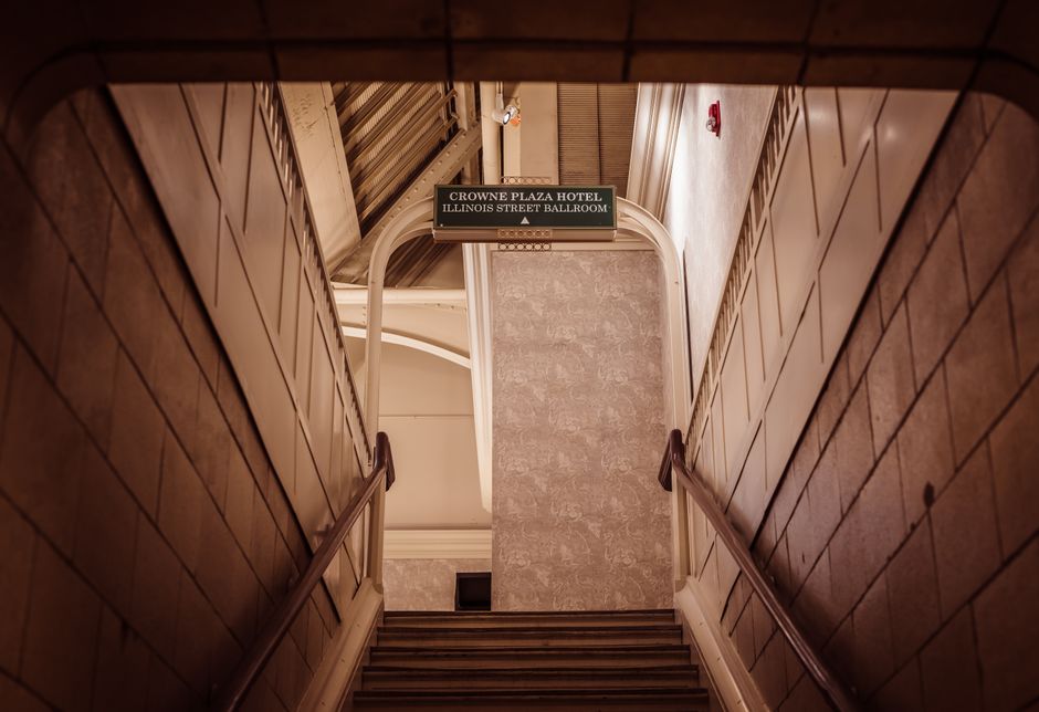 Escadaria interna de um hotel que leva ao salão de eventos, ilustrando um ambiente de hospedagem e eventos corporativos.