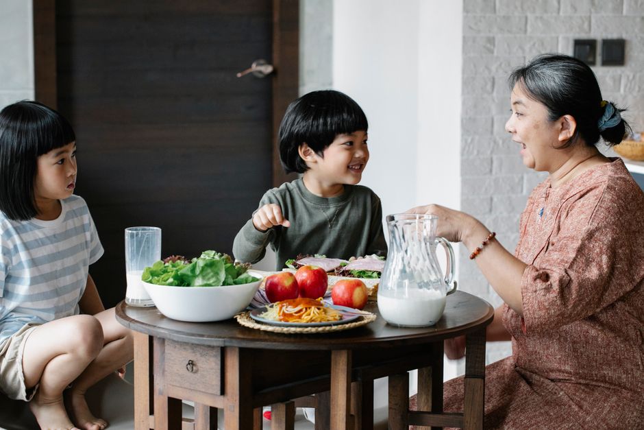 Uma mulher e duas crianças desfrutando de um café da manhã alegremente, simbolizando momentos familiares e nutrição.
