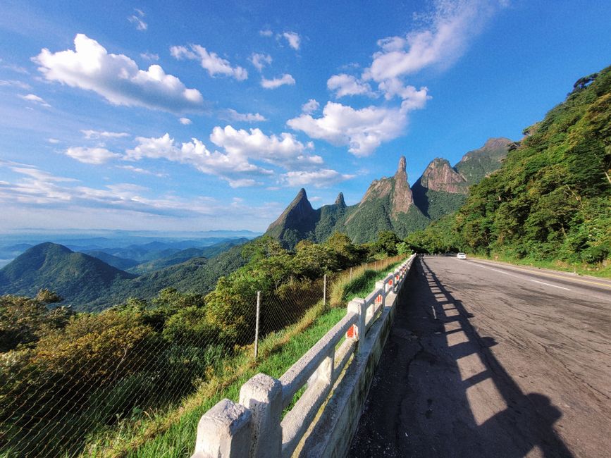 Estrada cercada por paisagens montanhosas e vegetação exuberante sob céu azul com nuvens, ideal para um artigo sobre natureza e turismo ao ar livre.