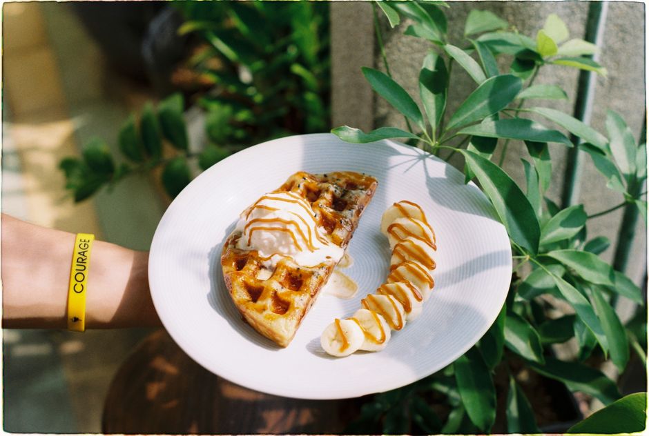 Pedaço de torta com sorvete e banana, servido ao ar livre em um ambiente com plantas