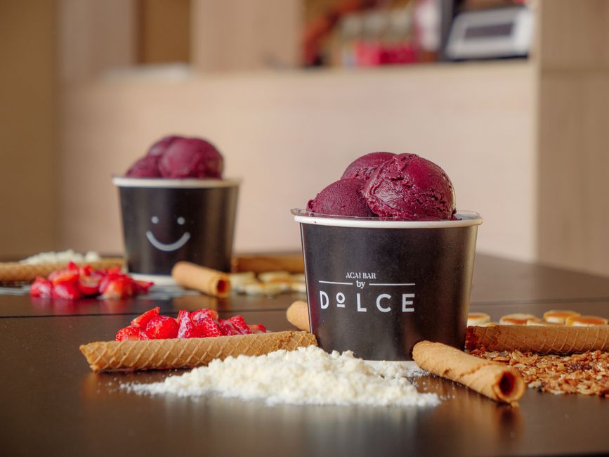 Duas taças de sorvete de açaí em um ambiente de café, decoradas com ingredientes como morangos, biscoitos e granulados, criando uma atmosfera convidativa para momentos de lazer.