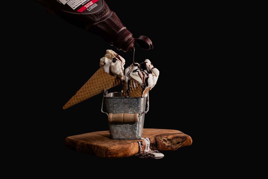 Foto de sorvete de casquinha sendo coberto por calda de chocolate, com um fundo preto que destaca a sobremesa.