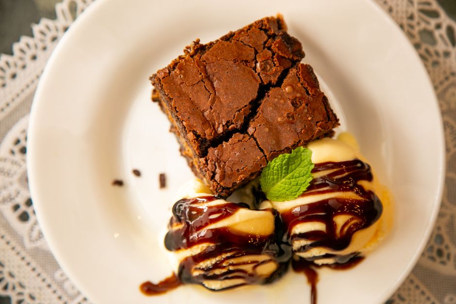Imagem de uma fatia de brownie acompanhada de sorvete com calda de chocolate, decorada com hortelã, servida em um prato branco para ilustrar sobremesas e gastronomia.
