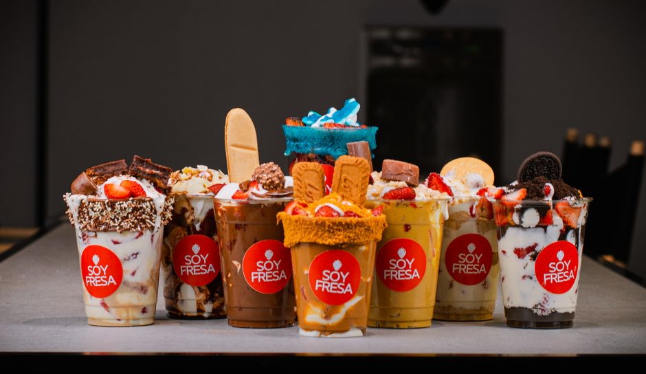Várias taças de sobremesas de iogurte com caldas, frutas e toppings decorativos, exibidas como destaque de um buffet ou loja de doces artesanais.