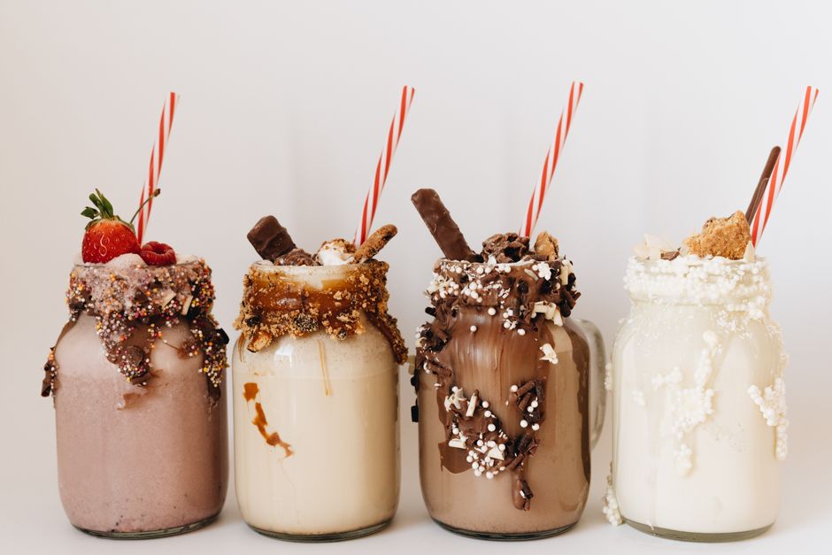 Quatro copos de milkshake decorados com diferentes coberturas, representando variedade de sabores e criatividade na gastronomia de sobremesas.