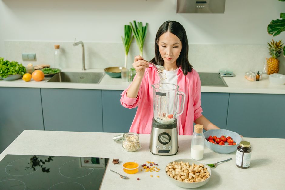 Mulher preparando um smoothie com ingredientes naturais na cozinha moderna, simbolizando saúde e bem-estar.