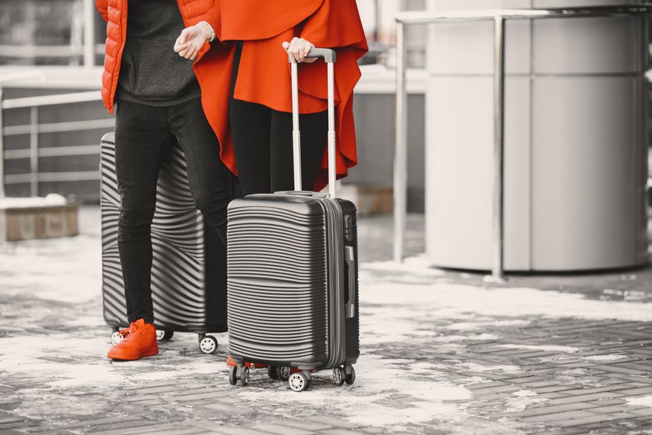 Imagem de duas pessoas com malas de rodinha, pronta para viagens, capturando o tema de deslocamento e turismo.