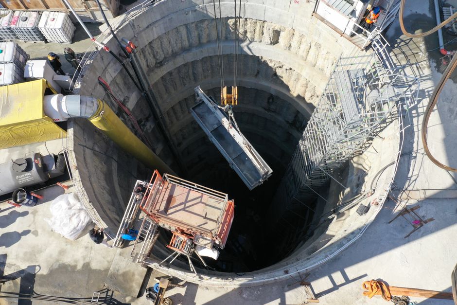 Visão aérea de um poço de construção em andamento, com equipamentos de elevação e estrutura de suporte ao redor.