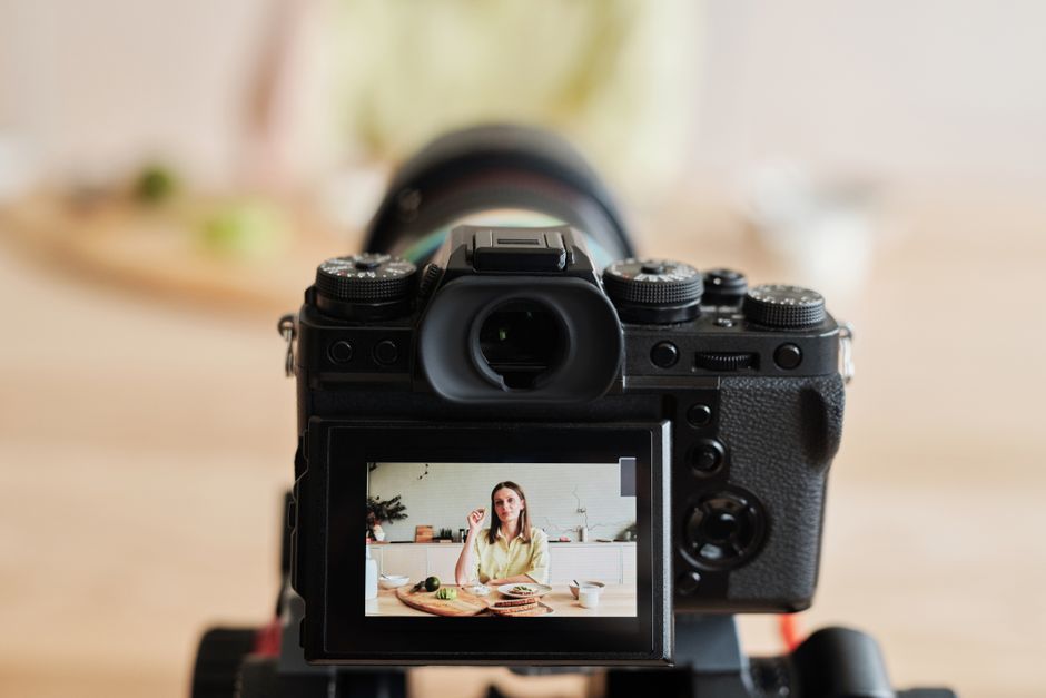 Câmera fotográfica capturando uma mulher em um ambiente de cozinha, ideal para um blog sobre produção de conteúdo ou audiovisual.