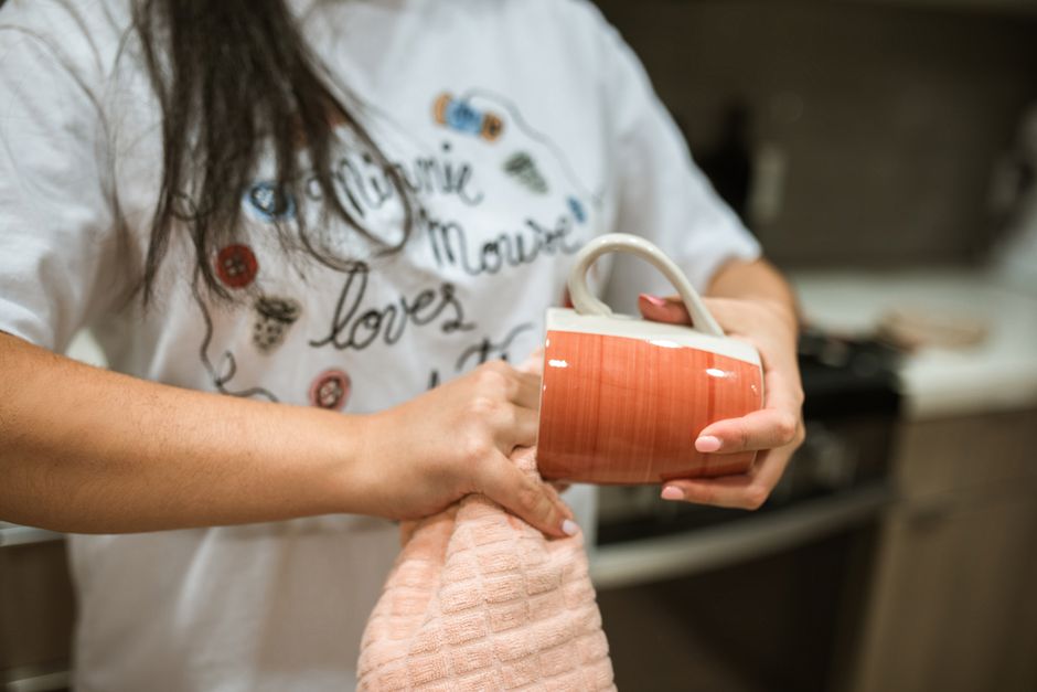 Pessoa segurando uma caneca de cerâmica na cozinha, simbolizando momentos de pausa e aconchego em casa.