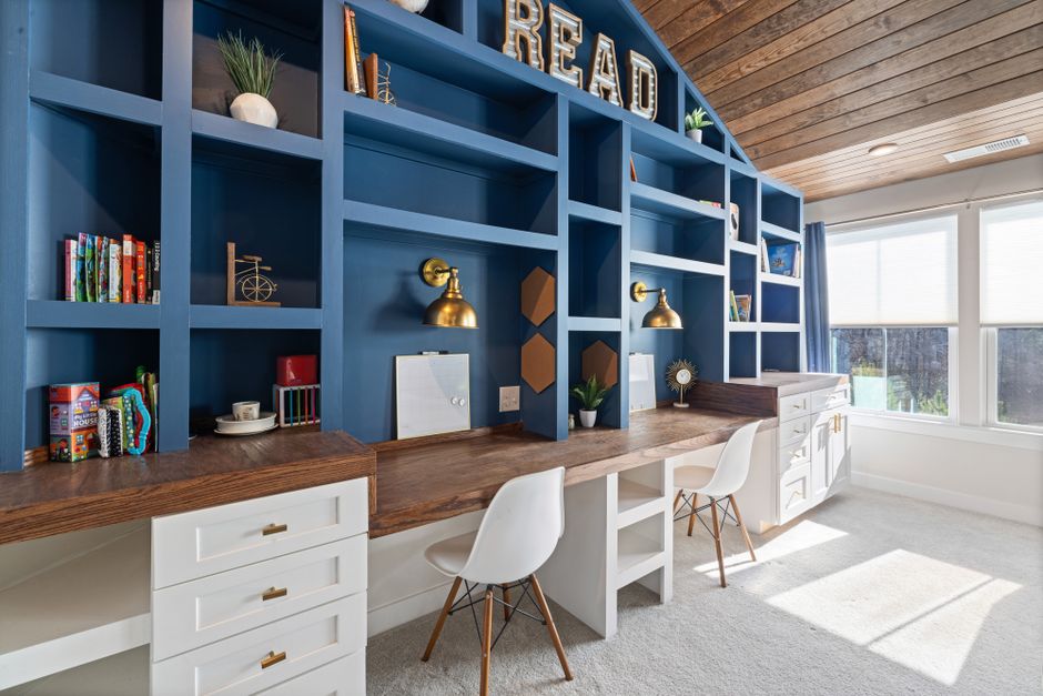 Escritório com estante azul decorada com livros, plantas e iluminação, ideal para ambientes de estudo ou trabalho em casa.