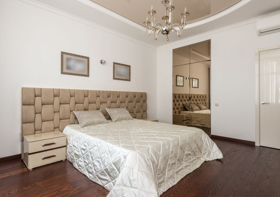 Quarto moderno com cama de tecido acolchoado, espelho de correr e decoração minimalista, ideal para artigos sobre design de interiores ou hospedagem de quartos de hotel.