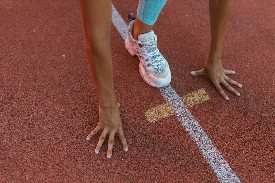 Imagem de uma pessoa preparada para começar uma corrida, posicionada na linha de saída de uma pista de atletismo, simbolizando início, competições ou preparação física.