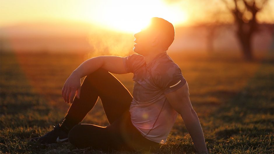 Homem sentado ao pôr do sol em um parque, relaxando e apreciando a natureza ao seu redor.
