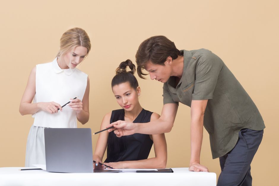 Três pessoas em uma reunião de trabalho, focadas em discutir projetos ou estratégias, com uso de um computador portátil.