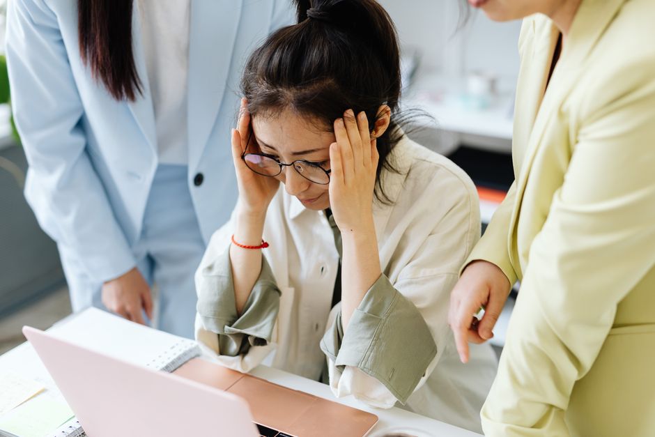 Mulher com expressão de estresse e frustração durante o trabalho, simbolizando pressão e dificuldades no ambiente profissional.