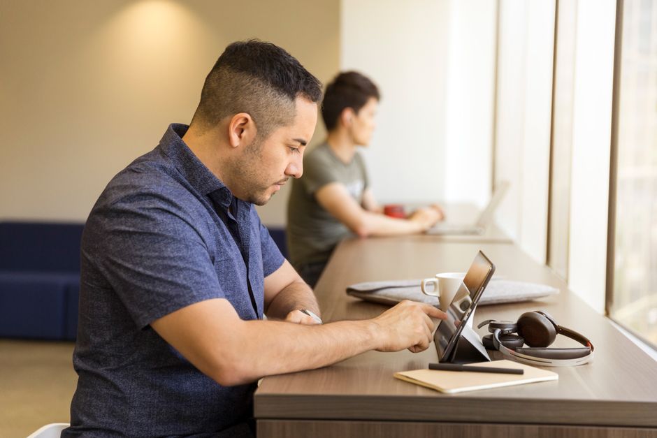 Homens concentrados em um espaço de coworking, utilizando dispositivos eletrônicos enquanto trabalham.