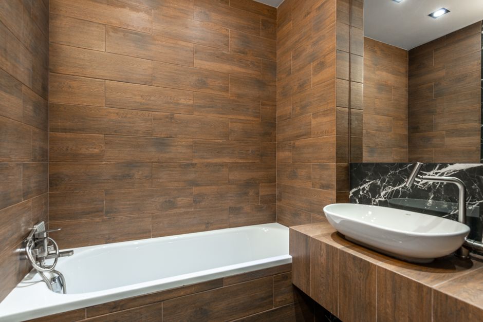 Banheiro moderno com revestimento de madeira, destaque para a banheira e a cuba de design elegante.