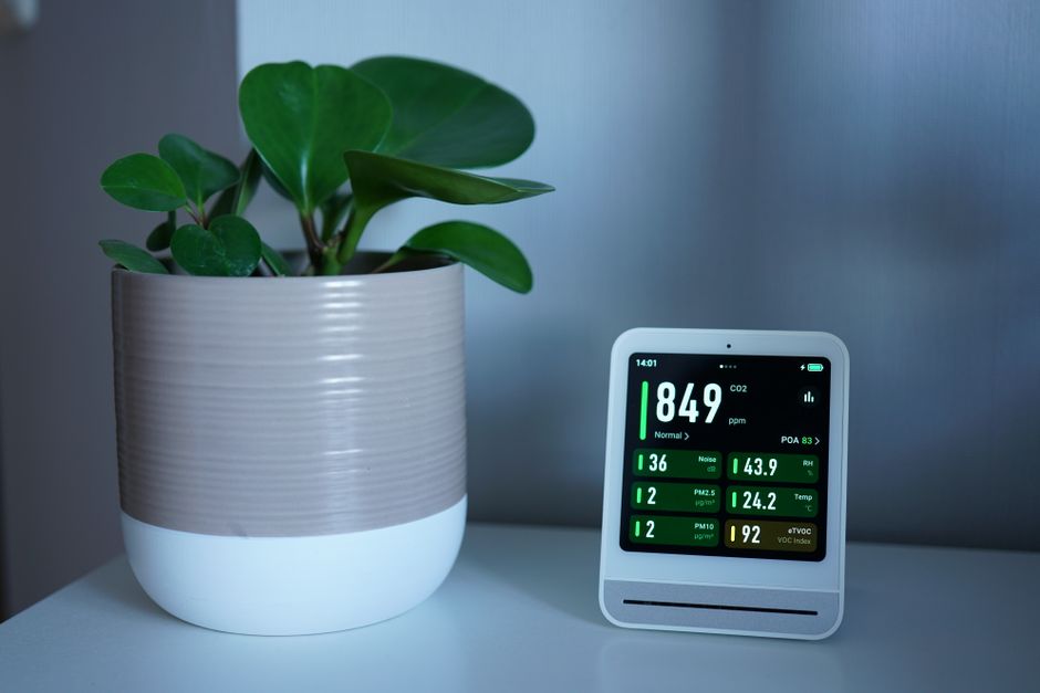 Imagem de um sensor de qualidade do ar ao lado de uma planta, simbolizando o cuidado com o ambiente e bem-estar no espaço de trabalho.