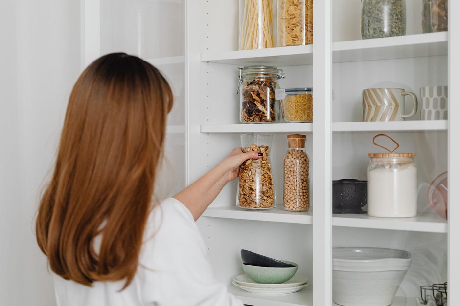 Mulher organizando despensa de alimentos em casa, focada em armazenamento e planejamento de ingredientes.