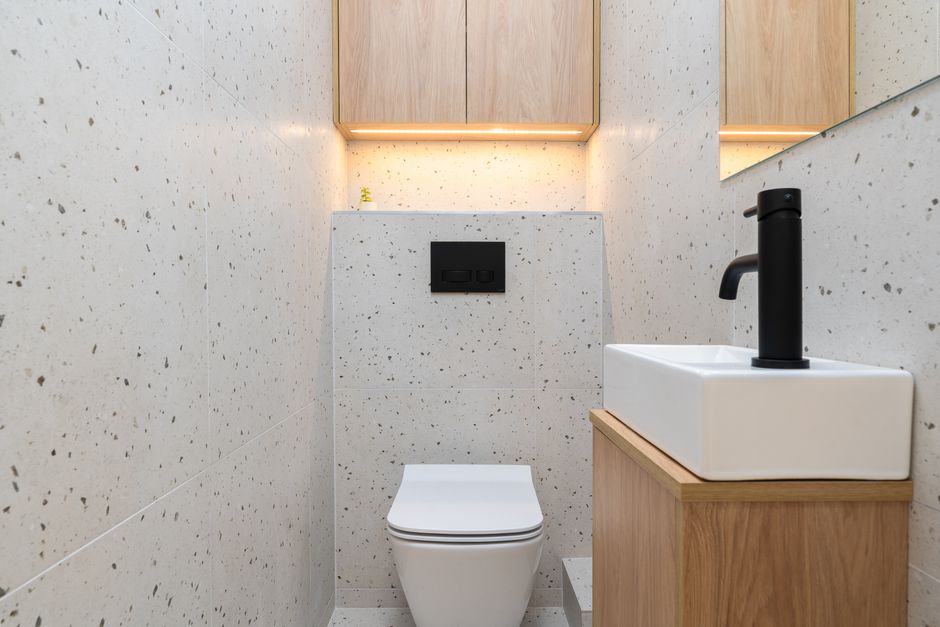 Banheiro moderno com acabamento minimalista, incluindo vaso sanitário e pequena pia com torneira preta, ideal para ambientes residenciais contemporâneos.
