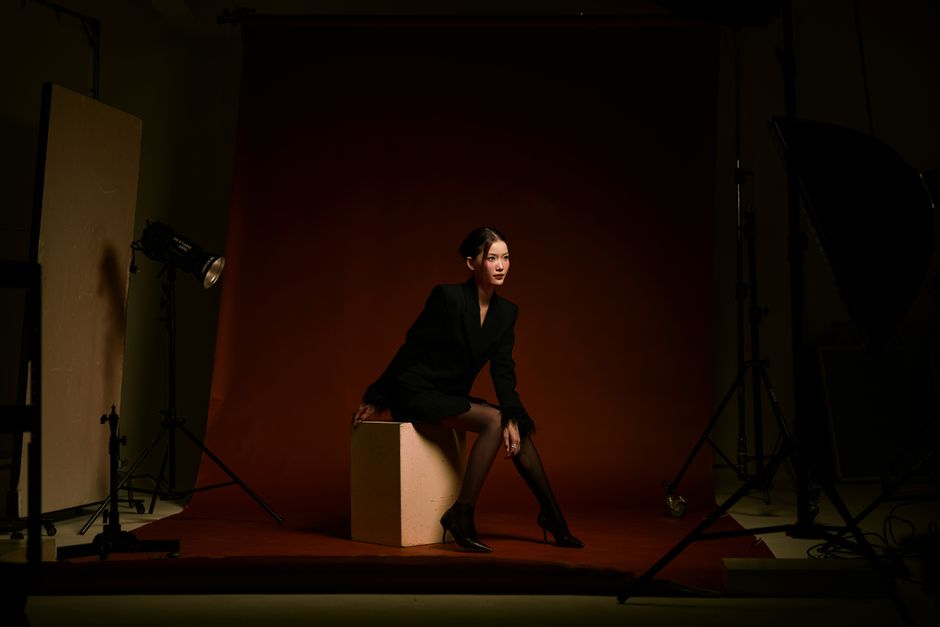 Mulher elegantemente vestida posando em um ensaio fotográfico com iluminação profissional e fundo de estúdio escuro.
