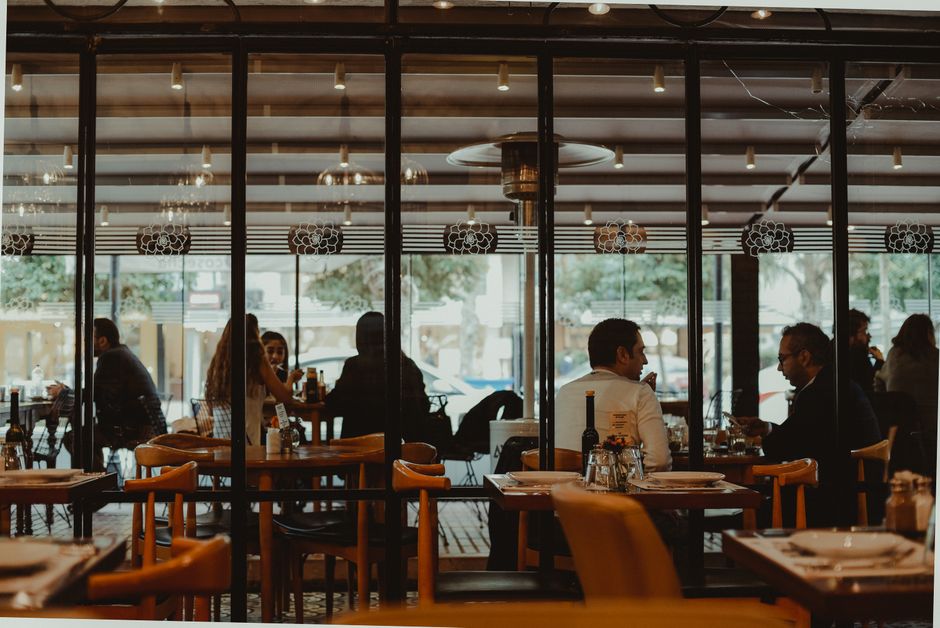 Imagem de um restaurante ou café com clientes conversando e aproveitando o ambiente interno e externo ao ar livre.