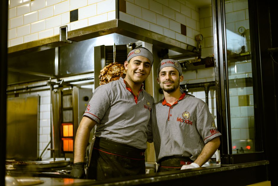 Dois funcionários de cozinha felizes posando juntos em um ambiente industrial de restaurante, demostrando trabalho em equipe e satisfação.