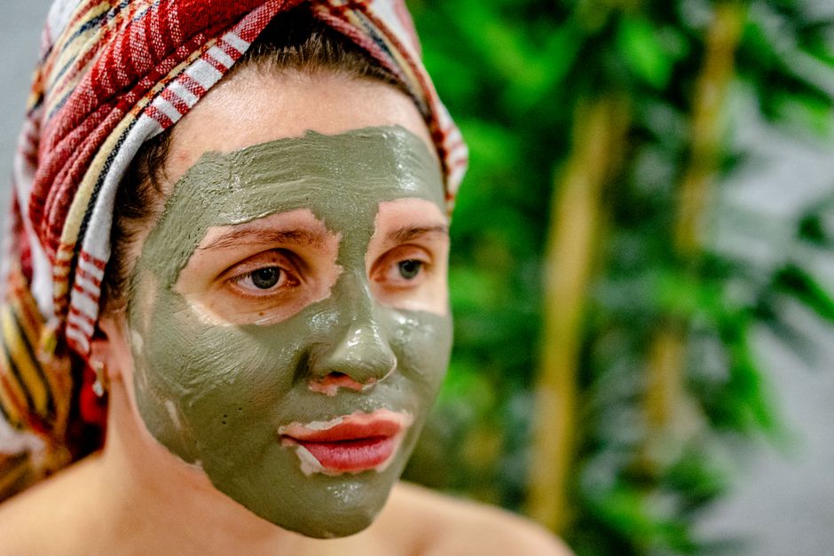 Mulher aplicando máscara facial de argila em um ambiente natural, representando cuidado com a pele e bem-estar pessoal.