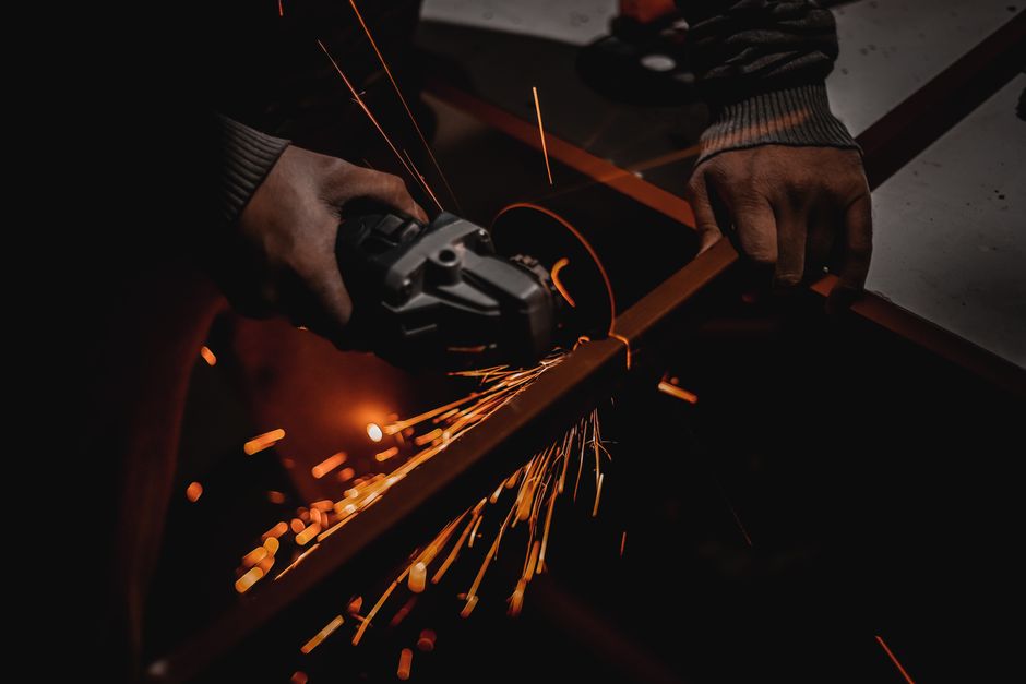 Imagem de um trabalhador usando uma serra circular para cortar uma peça de metal, destacando o processo de fabricação industrial.