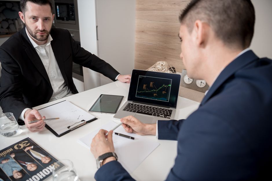 Dois homens de negócios discutindo estratégias e análises financeiras em uma reunião de escritório moderna.
