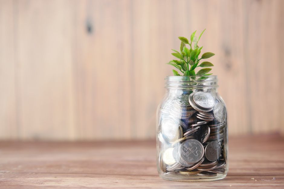 Imagem de um vidro com moedas de euro e uma planta crescendo no interior, simbolizando crescimento financeiro e sustentabilidade.