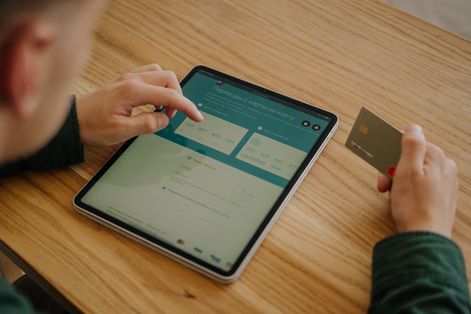 Pessoa realizando uma transação bancária digital usando tablet e cartão de crédito, com foco em tecnologia financeira e gerenciamento de contas online.