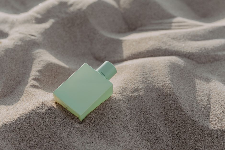 Frascos de perfume na areia, criando uma cena que evoca sensação de relaxamento e verão.