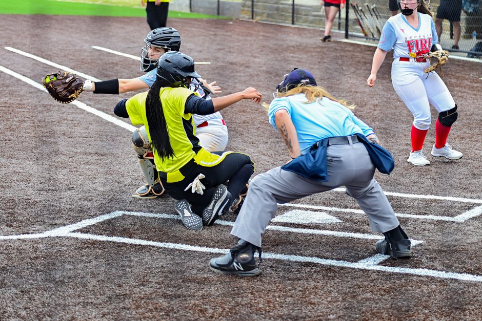 A cena de um jogo de beisebol infantil com jogadoras e uma árbitra em ação no campo.