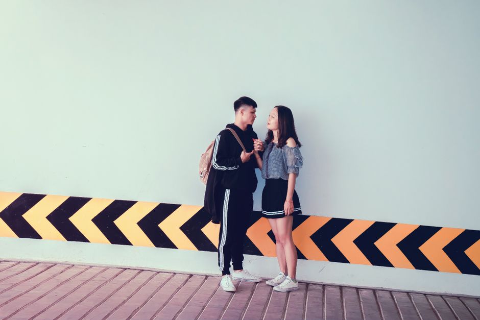 Dois adolescentes conversando de forma amigável ao lado de uma barreira laranja e preta, em um espaço urbano, refletindo uma interação social jovem.