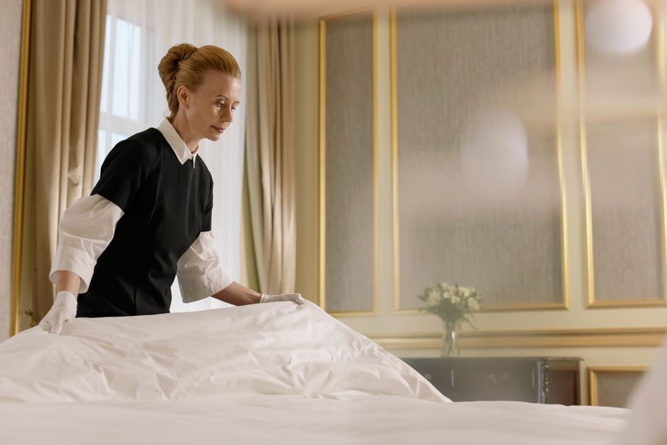 Mulher arrumando a cama em um ambiente elegante, transmitindo limpeza e cuidado com o espaço.