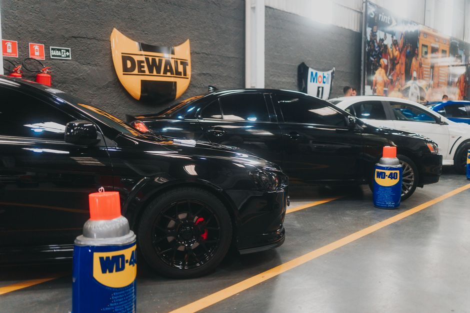 Carros pretos estacionados em uma oficina ou loja de automóveis, destaque para produtos de manutenção como WD-40 na foto.