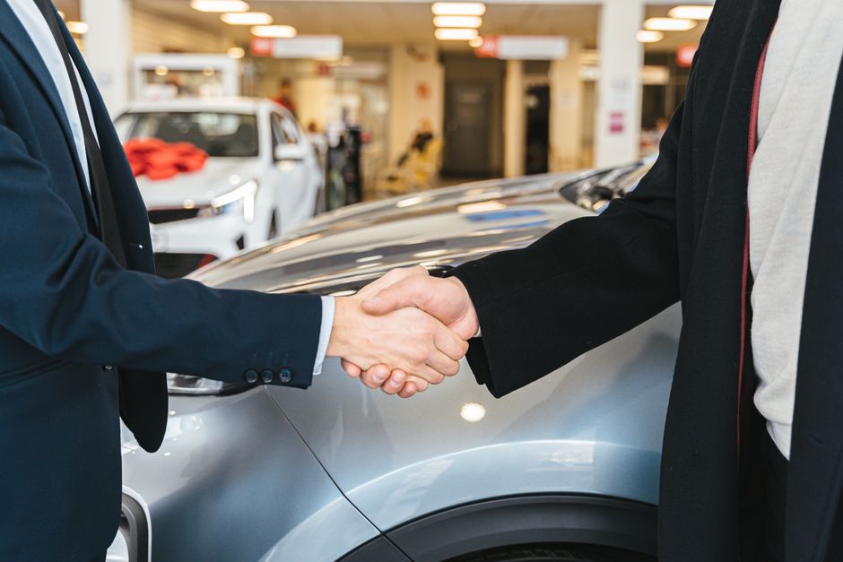 Duas pessoas realizando um aperto de mãos, simbolizando a assinatura de um acordo ou negócio de compra de carro em um concessionária.