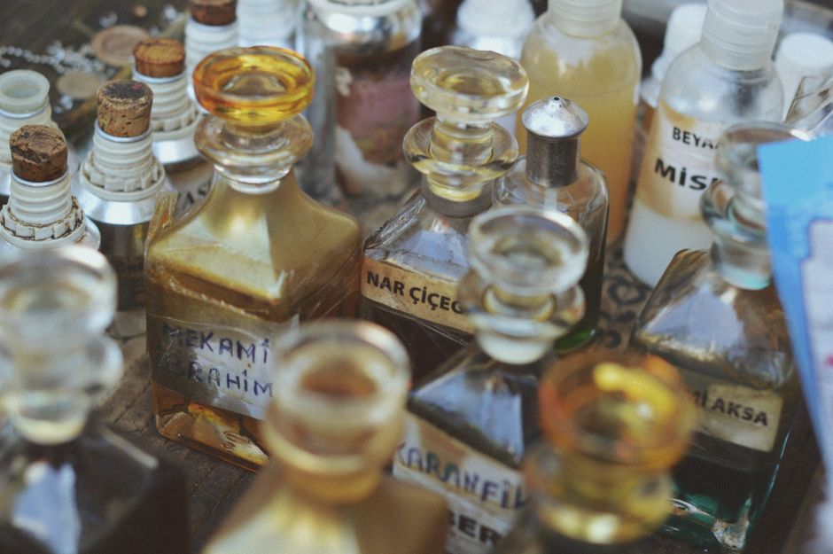 Imagem de uma coleção de frascos de perfume artesanais, com tampas de vidro coloridas e rótulos escritos à mão, representando a fabricação de fragrâncias caseiras.