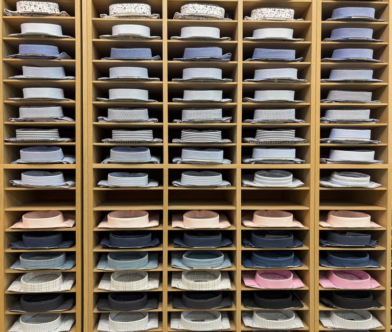 Prateleira repleta de camisas dobradas organizada por cores, ideal para mostrar organização e planejamento em um ambiente de armazenamento de roupas.