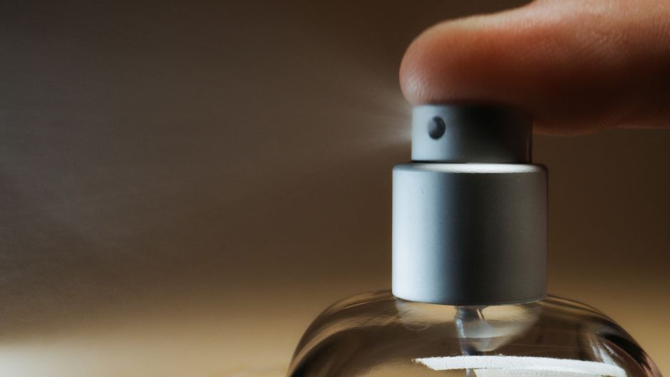 Pessoa apertando o spray de um frasco de vidro, possivelmente usando uma fragrância ou produto de higiene pessoal.