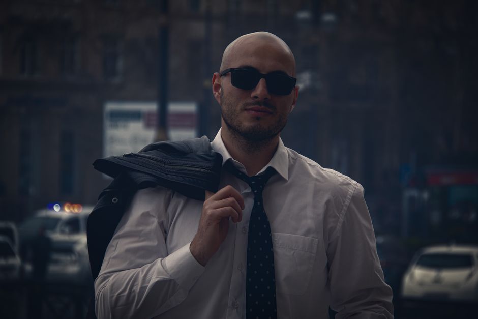 Homem estiloso com roupa formal, carregando uma mochila, pronto para o trabalho ou reunião, em ambiente urbano moderno.