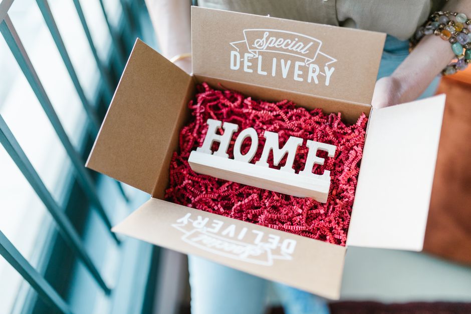 Caixa de entrega especial contendo uma plaque decorativa com a palavra 'HOME', ideal para artigos sobre entregas personalizadas e decorativas em ambiente doméstico.