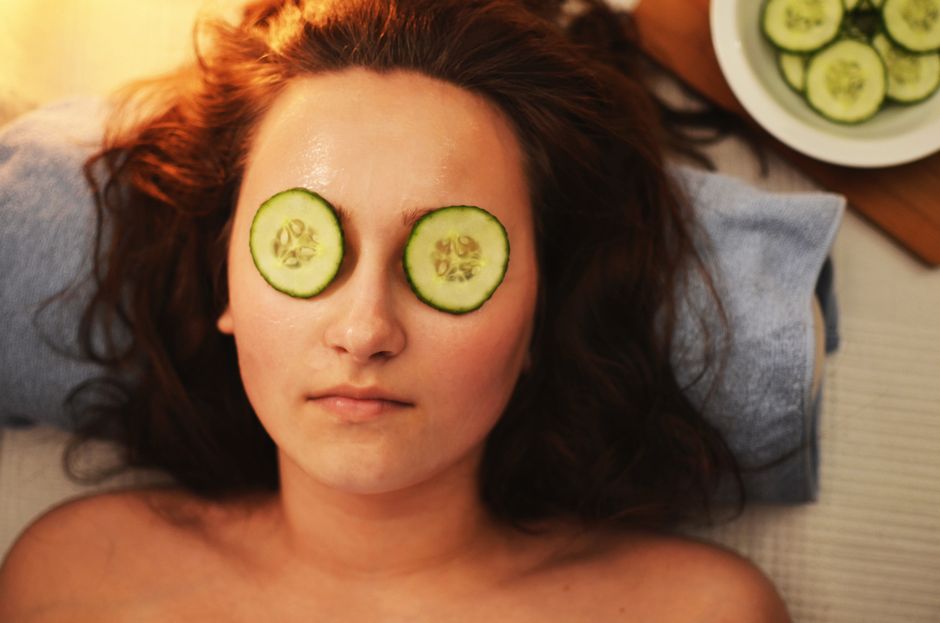 Mulher deitada com fatias de pepino sobre os olhos, praticando um tratamento de spa ou cuidados com a pele.