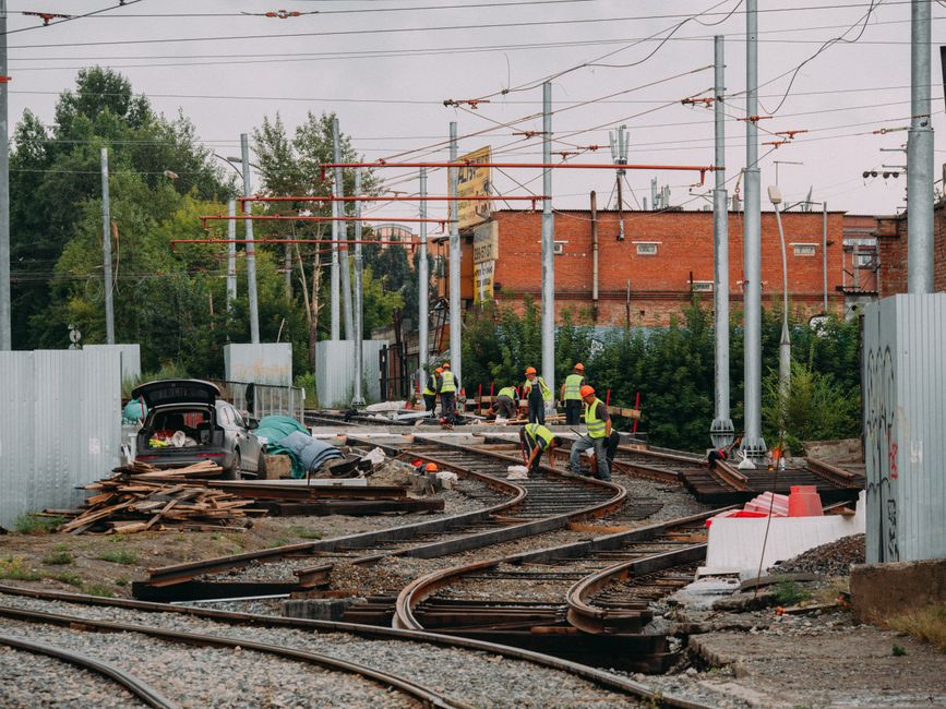 Funcionários trabalhando na construção e manutenção de trilhos de trem em uma área urbana com infraestrutura ferroviária e componentes elétricos.