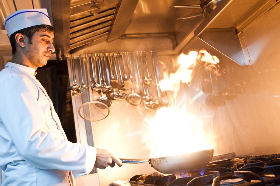 Chef cozinheiro ajustando fogo alto em uma panela no fogão durante preparo de pratos na cozinha de um restaurante.
