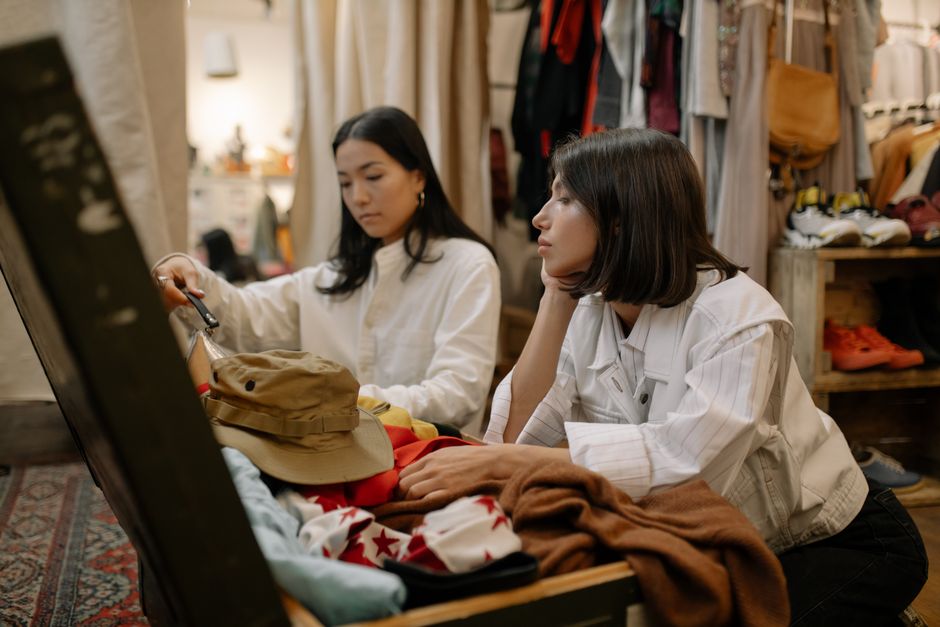 Duas mulheres avaliando roupas em uma loja de segunda mão, focando no consumo consciente e moda sustentável.